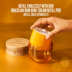 A hand inserts an orange-yellow cream refill pod into a clear amber jar, with a branded wooden lid beside it on a warm orange background. Text at the top reads: 'REFILL ENDLESSLY WITH OUR BRAZILIAN BUM BUM CREAM REFILL POD (REFILL SOLD SEPARATELY)'.