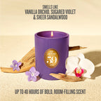 A purple jar candle with a lit flame and a gold circular label reading '59 SCENTS' is styled on a beige surface with dried wood pieces, purple flowers, and a white orchid. Text above says 'SMELLS LIKE VANILLA Orchid, SUGARED VIOLET & SHEER SANDALWOOD' and text below says 'UP TO 40 HOURS OF BOLD, ROOM-FILLING SCENT'.