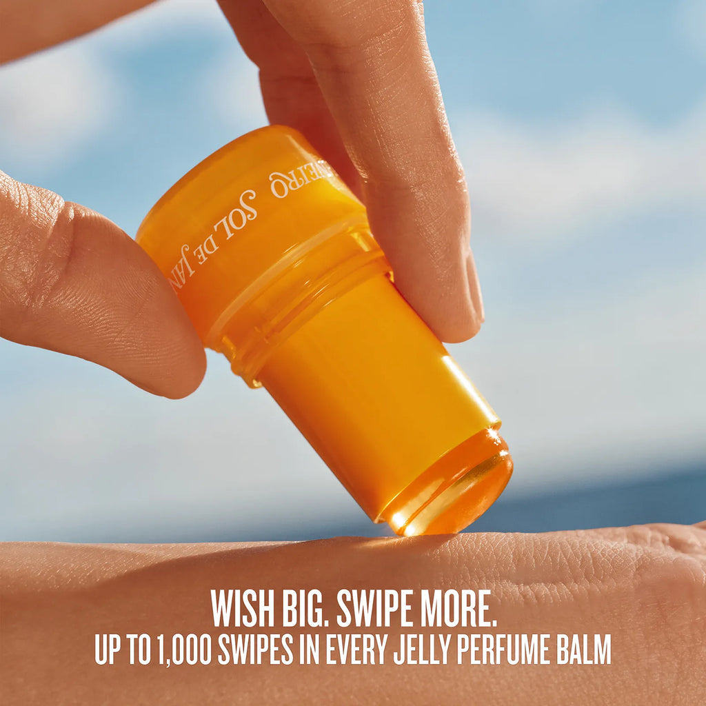 Person applying a yellow sunscreen stick on their arm with a blue sky background