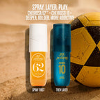 Two Sol Janeiro Cheiroso sunscreen bottles standing upright on a sandy beach-style background next to a yellow soccer ball. White text at the top reads 'SPRAY.