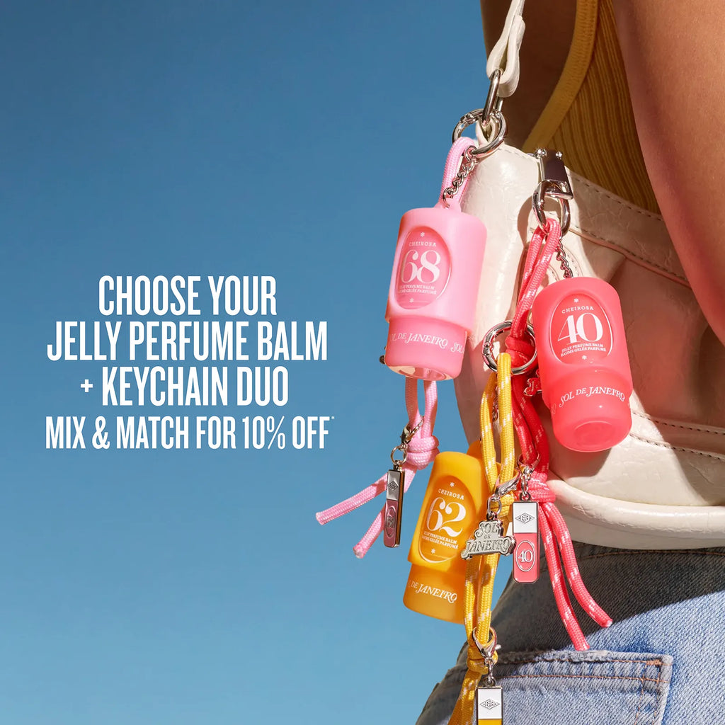 A close-up lifestyle shot of a person carrying a cream-colored shoulder bag with three colorful jelly perfume balm keychain bags attached. The bags are pink, coral red, and yellow, each with a small round bottle, keychain, and dangling charms.