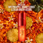 A red and orange cylindrical bottle of Sol Janeiro Intense sunscreen stands centered against a tropical background of sliced pineapple, white flowers, and amber liquid. White text at the top reads, 'SMELLS LIKE RIPE PINEAPPLE, ORANGE FLOWER & SOLAR AMBERY ACCORD.