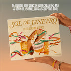 A person holds a boxed body care set labeled SOL DE JANEIRO against a soft beige-to-gray gradient background. The box features illustrated products including a body cream jar, body oil bottle, and a sculpting tool, with colorful ribbon graphics and the text 'FEATURING MIDI SIZES OF BODY CREAM (75 ML) & BODY OIL (58 ML), PLUS A SCULPTING TOOL.